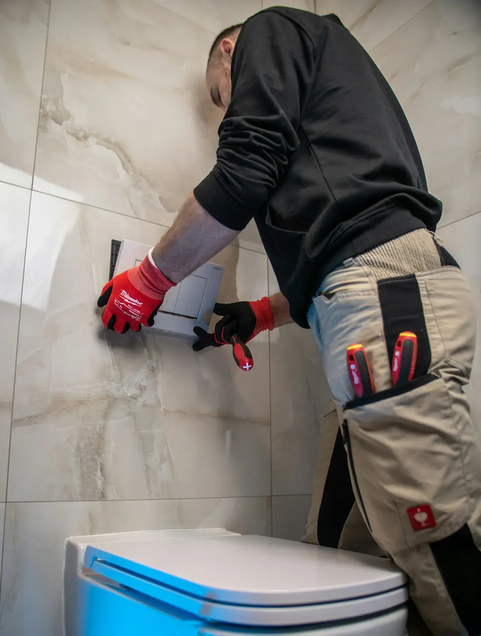 Plumber repairing a toilet in a tiled bathroom