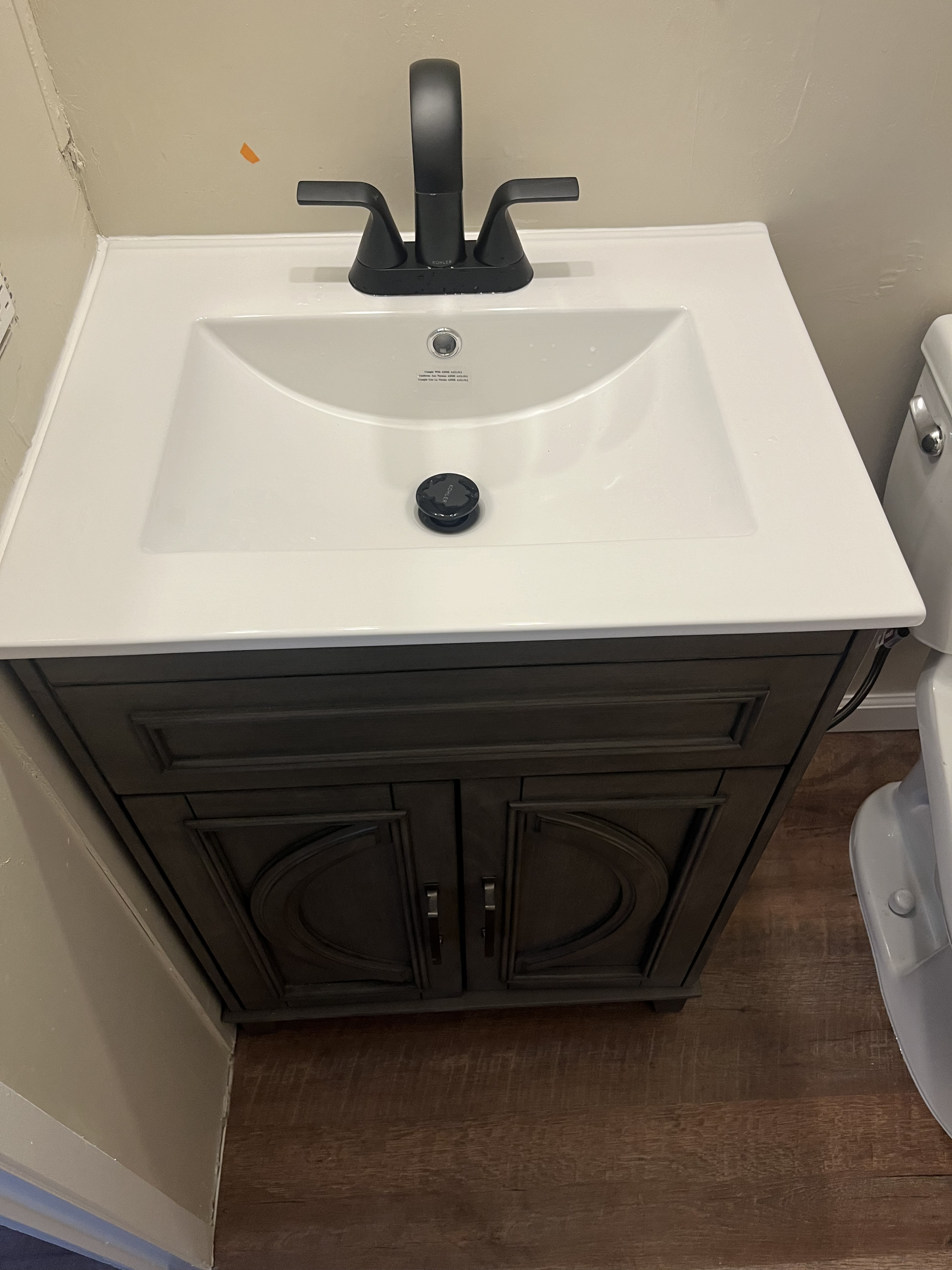 A newly installed dark gray vanity with a white integrated sink and a matte black faucet is shown in a bathroom.